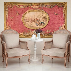 May include: Two antique wooden armchairs with beige cushions and cane backs flank a small white table. A large tapestry with a pink background and a central oval painting hangs on the wall, creating a classic, elegant living room setting.