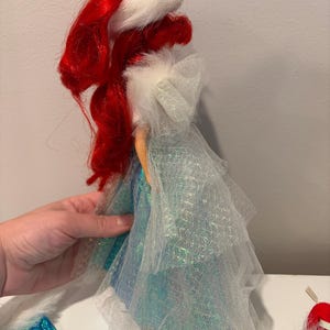 Puede incluir: Mu&ntilde;eca con cabello rojo y sombrero con borde de piel blanca. La mu&ntilde;eca viste un vestido azul y blanco con una capa transparente. Un objeto de colecci&oacute;n.