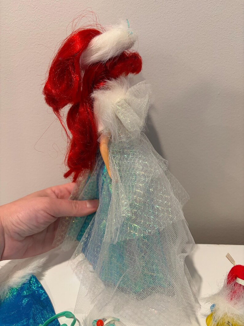 Puede incluir: Mu&ntilde;eca con cabello rojo y sombrero con borde de piel blanca. La mu&ntilde;eca viste un vestido azul y blanco con una capa transparente. Un objeto de colecci&oacute;n.