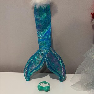 Puede incluir: Un conjunto de disfraz de sirena con una cola iridiscente de color verde azulado con un ribete blanco y esponjoso y una peque&ntilde;a parte superior verde. La cola mide aproximadamente 30 cm de largo. Ideal para disfraces o fiestas tem&aacute;ticas.