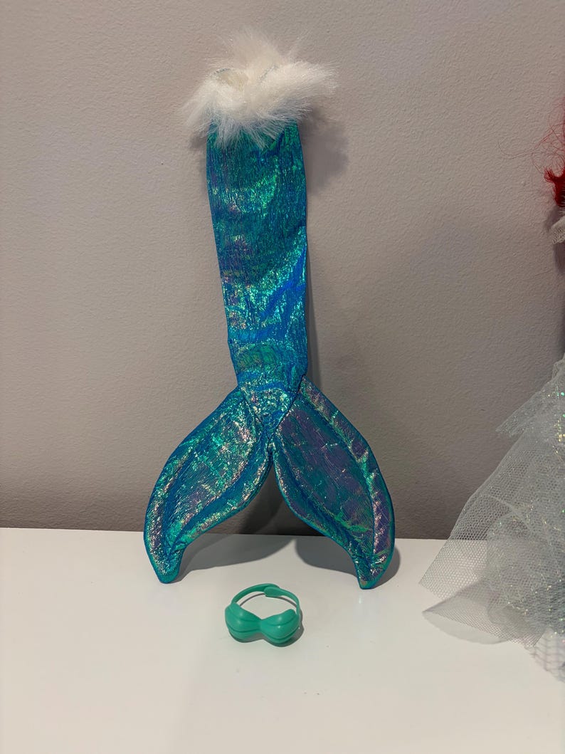 Puede incluir: Un conjunto de disfraz de sirena con una cola iridiscente de color verde azulado con un ribete blanco y esponjoso y una peque&ntilde;a parte superior verde. La cola mide aproximadamente 30 cm de largo. Ideal para disfraces o fiestas tem&aacute;ticas.