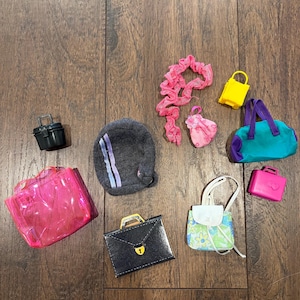 May include: A collection of miniature doll accessories, including a black suitcase, a pink transparent tote bag, a gray backpack, and a teal and purple duffel bag. Other items include a yellow purse, a pink purse, and a small white and floral bag.