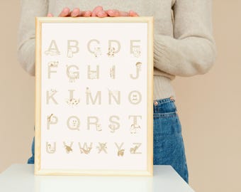 Puede incluir: Un marco de madera rectangular que contiene un póster del alfabeto con letras beige de la A a la Z. Cada letra se combina con una pequeña ilustración de líneas de color marrón claro de un animal u objeto, como un gato para la A, un pájaro para la G y una cebra para la Z.