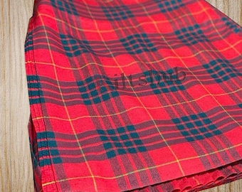 May include: Folded red plaid fabric with a teal and yellow grid pattern. The fabric has a woven texture and the text "KiltsHub" is visible. The fabric is folded and appears to be a kilt or similar garment.