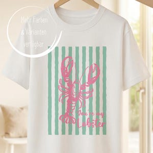 Könnte beinhalten: Ein weißes T-Shirt mit kurzen Ärmeln und einem Grafikdruck eines rosafarbenen Hummers, der über vertikalen mintgrünen Streifen zentriert ist. Der Text "You're my Lobster" ist in rosa Schreibschrift unter dem Hummer aufgedruckt.