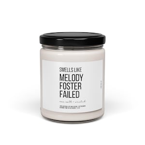 Peut inclure: Une bougie blanche dans un pot en verre avec un couvercle noir. L'étiquette indique "SMELLS LIKE MELODY FOSTER FAILED" avec "sea salt + orchid" en dessous. La bougie est faite d'un mélange de cire de soja naturelle et d'une mèche en coton.