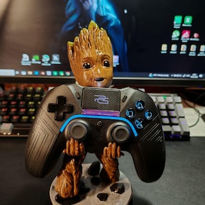 May include: A brown, tree-like character figurine standing on a circular base, holding a black video game controller. The controller features a central touchpad with a purple logo, a blue light bar, and standard directional buttons and joysticks.