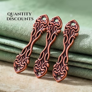 May include: Three elongated copper-toned metal charms featuring an intricate openwork scroll and leaf pattern. Each charm has a small circular hole at the top and bottom for attachment. The text QUANTITY DISCOUNTS is visible in the upper left corner.