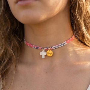 Peut inclure: Un collier ras du cou à motifs floraux avec un pendentif en forme de croix blanche et un pendentif disque doré gravé du nom "Margot". Le collier présente un motif floral rose et blanc.