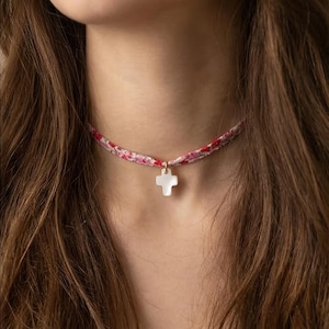 Peut inclure: Un collier délicat avec un pendentif en forme de croix blanche suspendu à un ras du cou à motifs floraux. Le ras du cou présente un mélange de rouge, de rose et de blanc, créant une esthétique douce et féminine. Le pendentif en forme de croix est petit et simple.