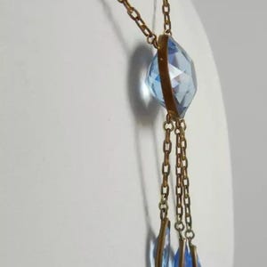 May include: A gold chain necklace with a large, faceted, light blue crystal pendant. The pendant is attached to three smaller, teardrop-shaped, light blue crystals.