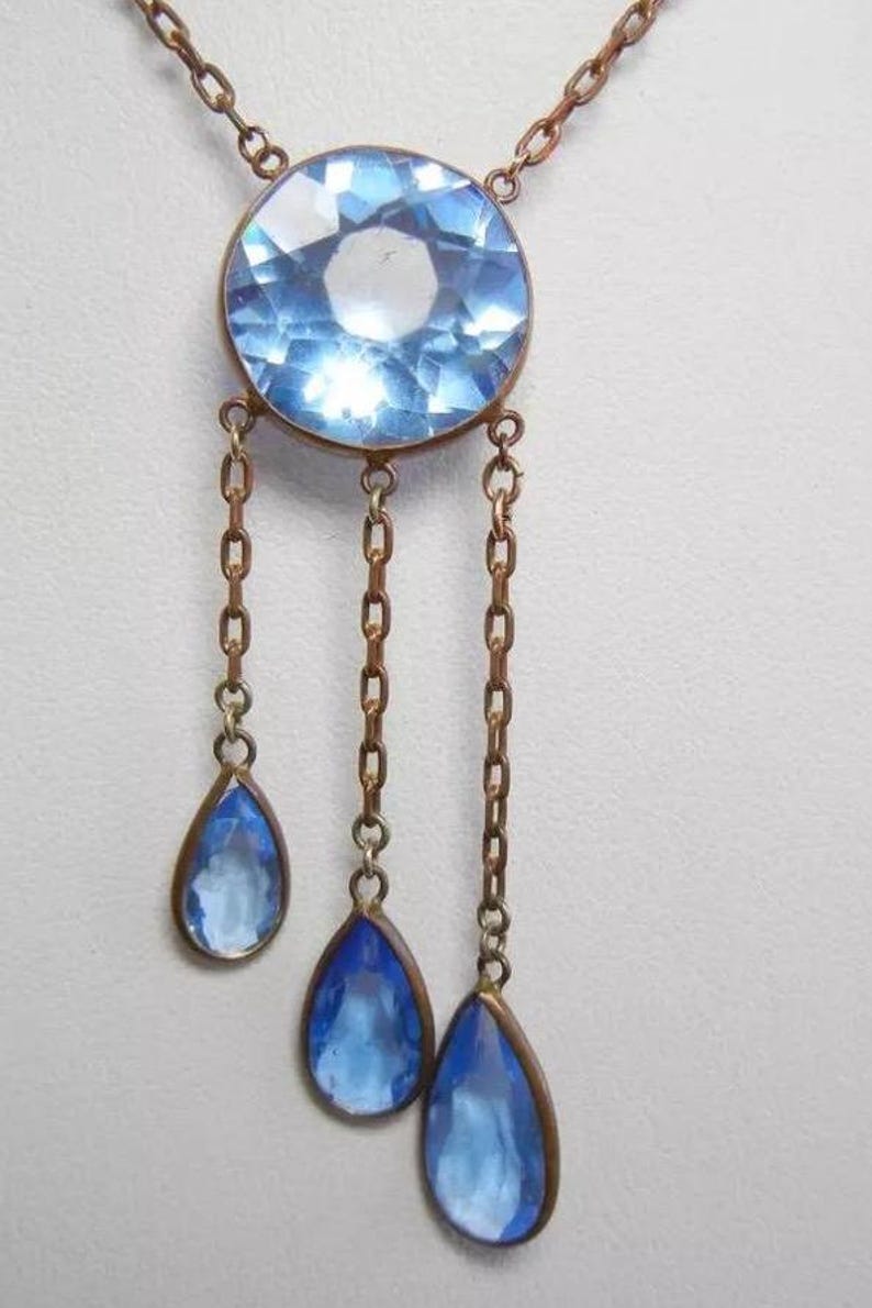 May include: A vintage necklace with a large, round, light blue crystal pendant and three smaller teardrop-shaped crystals hanging from chains.