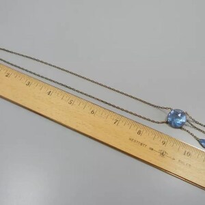 May include: A silver chain necklace with a blue glass pendant featuring a large round stone and three teardrop-shaped stones.
