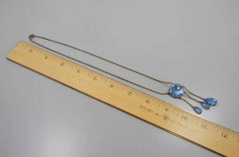 May include: A silver chain necklace with a blue glass pendant featuring a large round stone and three teardrop-shaped stones.