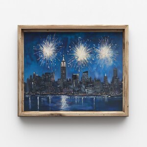 Può includere: Dipinto incorniciato dello skyline di New York City di notte, con fuochi d'artificio sopra. L'Empire State Building è in evidenza. L'opera d'arte è ambientata su uno sfondo di cielo blu scuro e si riflette nell'acqua.