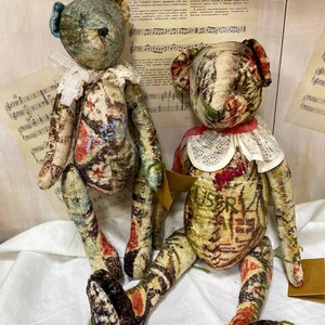 Puede incluir: Dos osos de peluche hechos a mano con tela de estilo vintage. Uno tiene una oreja azul y un cuello de encaje blanco, el otro tiene una cinta roja y un cuello de encaje blanco. Los osos tienen estampados en tonos marrones, rojos y verdes.