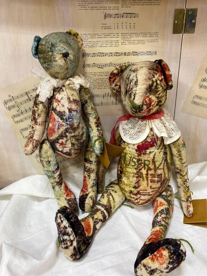 Puede incluir: Dos osos de peluche hechos a mano con tela de estilo vintage. Uno tiene una oreja azul y un cuello de encaje blanco, el otro tiene una cinta roja y un cuello de encaje blanco. Los osos tienen estampados en tonos marrones, rojos y verdes.