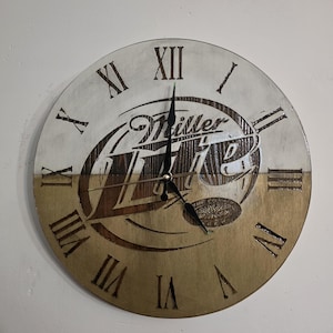 May include: A round wooden clock with a two-tone design. The top half is painted white, and the bottom half is stained brown. The clock face features Roman numerals and the "Miller Lite" logo. The clock hands are black.