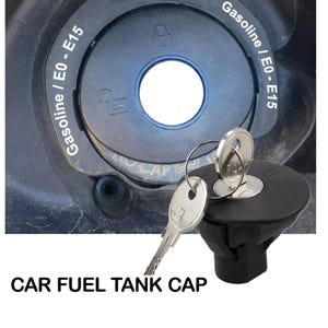 May include: A black locking car fuel tank cap with two silver metal keys inserted. The cap features a circular design with a keyhole in the center. The background shows a vehicle fuel filler neck with text reading Gasoline / E0 - E15.