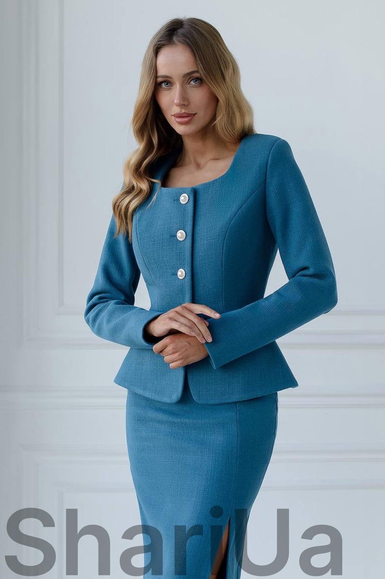 May include: A teal two-piece suit featuring a fitted jacket with a square neckline, three white buttons, and a peplum waist. The matching pencil skirt completes the professional ensemble. The text "Shari Ja" is visible at the bottom.