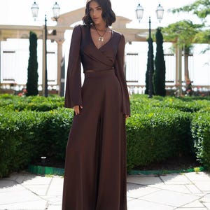 May include: A brown two-piece outfit featuring a wrap-style long-sleeve top and wide-leg pants. The top has a V-neck and flared sleeves. The outfit is made of a flowing fabric and is suitable for formal occasions.
