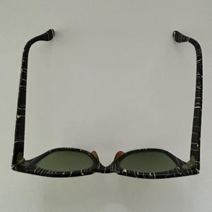 May include: Sunglasses with a black and white marbled pattern frame and green lenses. The sunglasses have a classic design with a keyhole bridge and curved temples. The frame is made of a durable material.
