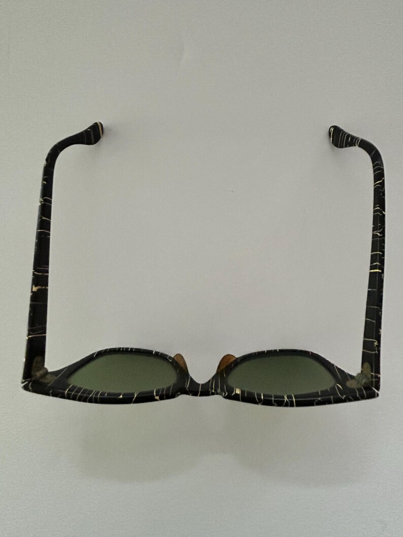 May include: Sunglasses with a black and white marbled pattern frame and green lenses. The sunglasses have a classic design with a keyhole bridge and curved temples. The frame is made of a durable material.
