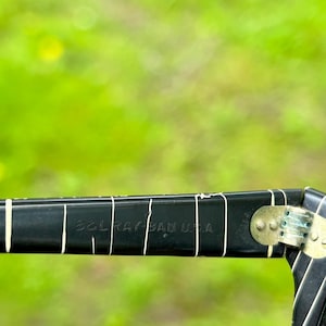 May include: Close-up of a black Ray-Ban USA sunglasses arm. The arm has white vertical lines and the text "B&L RAY BAN USA" in white. The hinge is gold-colored.