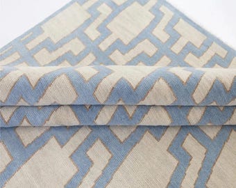 May include: A folded textile with a geometric pattern. The design features light blue and beige shapes outlined in a darker beige color. The fabric is folded over, revealing the pattern and texture.