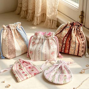 Puede incluir: Cinco bolsas de tela con cordón que presentan varios patrones florales y de rayas en tonos rosa, crema, marrón y azul. Las bolsas tienen partes superiores fruncidas con cierres de cordón o cinta a juego, mostrando intrincados estampados.
