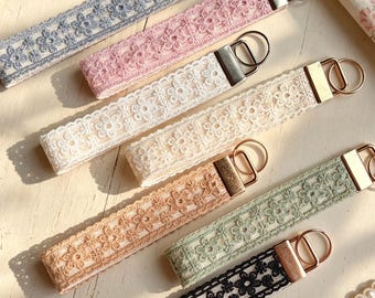 Peut inclure: Un ensemble de six porte-clés en tissu rectangulaires ornés de motifs de dentelle florale en bleu, rose, crème, beige, vert sauge et noir. Chaque sangle est fixée par une pince en métal argenté et un anneau brisé circulaire pour les clés.