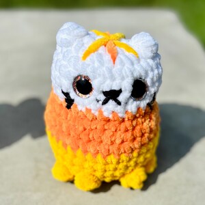 A white, orange, and yellow cat in candy corn colors with glitter eyes, a black mouth, nose, and whiskers