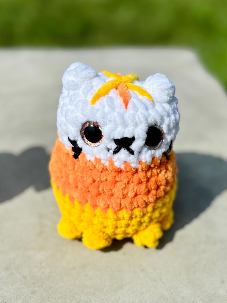 A white, orange, and yellow cat in candy corn colors with glitter eyes, a black mouth, nose, and whiskers