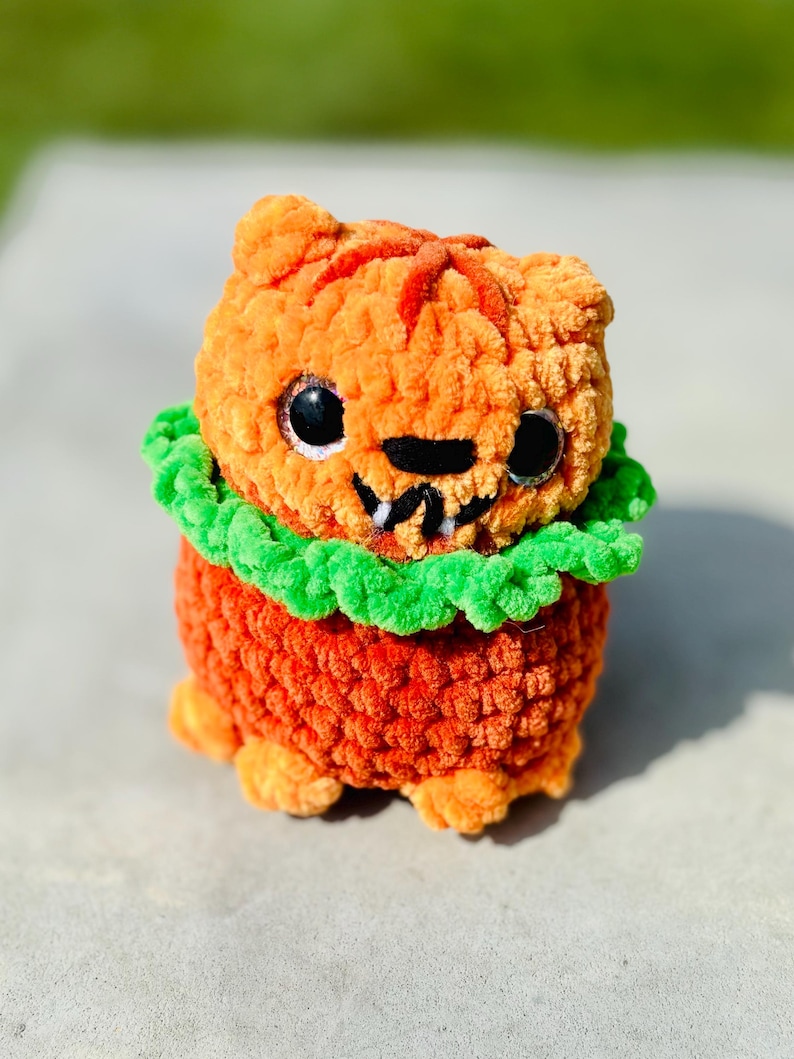 Handmade pumpkin cat for Halloween. Cat has bright orange yarn, bright sparkling eyes, and a green collar around its neck.