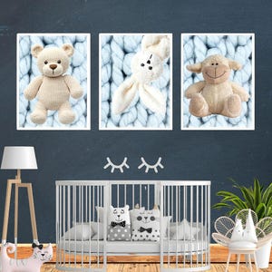 May include: Three framed prints of a teddy bear, a bunny, and a lamb, set against a light blue knitted background. Below, a white cot with decorative pillows and a cat-shaped nightstand. A wooden floor lamp and a chair with a bunny-shaped back complete the nursery decor.