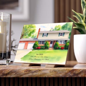May include: A personalized house portrait on a wooden block, featuring a two-story home with a red brick garage and green landscaping. The text "Est. 2025 The Johnsons' New Home Where Memories Are Made" is displayed.