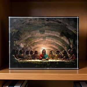 Op de afbeelding: Een ingelijste prent van "Het Laatste Avondmaal" toont Jezus en zijn discipelen aan een tafel. Het kunstwerk speelt zich af in een stenen gewelfde kamer met een lichtbron die het midden verlicht. De figuren dragen gewaden en de tafel is gedekt met voedsel.