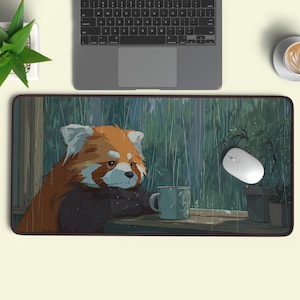 May include: A rectangular mouse mat with an illustration of a red panda with a mug, looking out at the rain. The mat has a dark border and a light green background with rain and plants.