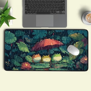Puede incluir: Alfombrilla de ratón rectangular con una ilustración de tres ranas bajo un paraguas rojo en una escena de lluvia. El diseño incluye hojas verdes grandes, flores de loto y un ratón blanco.