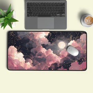 Puede incluir: Alfombrilla de ratón rectangular con un diseño de cielo nocturno de ensueño con nubes rosas y moradas, una luna llena y detalles dorados. Un ratón de ordenador blanco descansa sobre la alfombrilla, junto a un portátil.