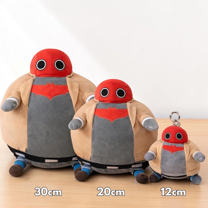 May include: Three plush figures of a character with a red head and large black eyes, wearing a tan jacket and gray shirt with a red emblem. The largest is 30cm tall, the middle one is 20cm, and the smallest is 12cm and a keychain.