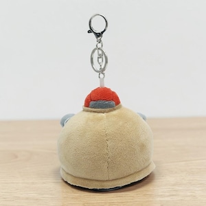 May include: A plush keychain in the shape of a round, tan creature with a red hat and gray accents. The keychain has a silver metal clasp and chain. The plush toy is soft and cuddly.