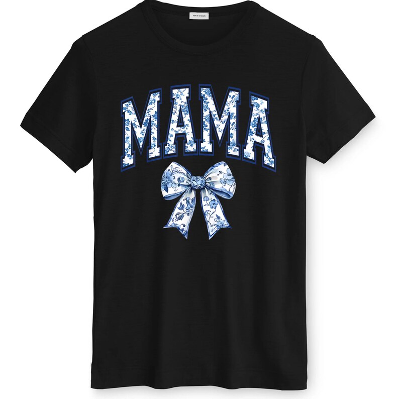 May include: Black t-shirt featuring the word "MAMA" in a blue and white floral design, arched across the chest. A matching floral bow is positioned below the word. The shirt has a crew neck and short sleeves.