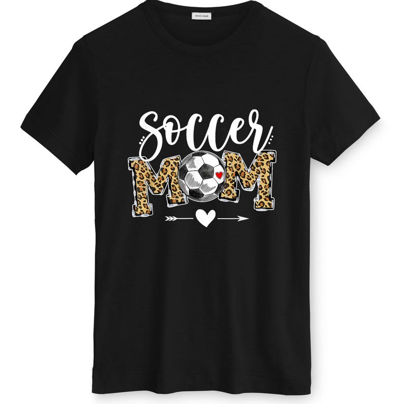 May include: Black t-shirt with the words "Soccer Mom" in white script and leopard print block letters. A soccer ball with a red heart is in the center. A white heart and arrow design are below the text.
