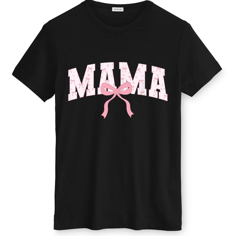 May include: Black crew neck t-shirt featuring the word "MAMA" in white, filled with pink bows. A large pink bow is positioned below the word. The shirt is a casual style.
