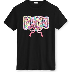 May include: Black t-shirt with the word "MAMA" in a colourful, floral design. The word is in a bubble letter style with a pink bow. The shirt is a classic crew neck style, suitable for casual wear.