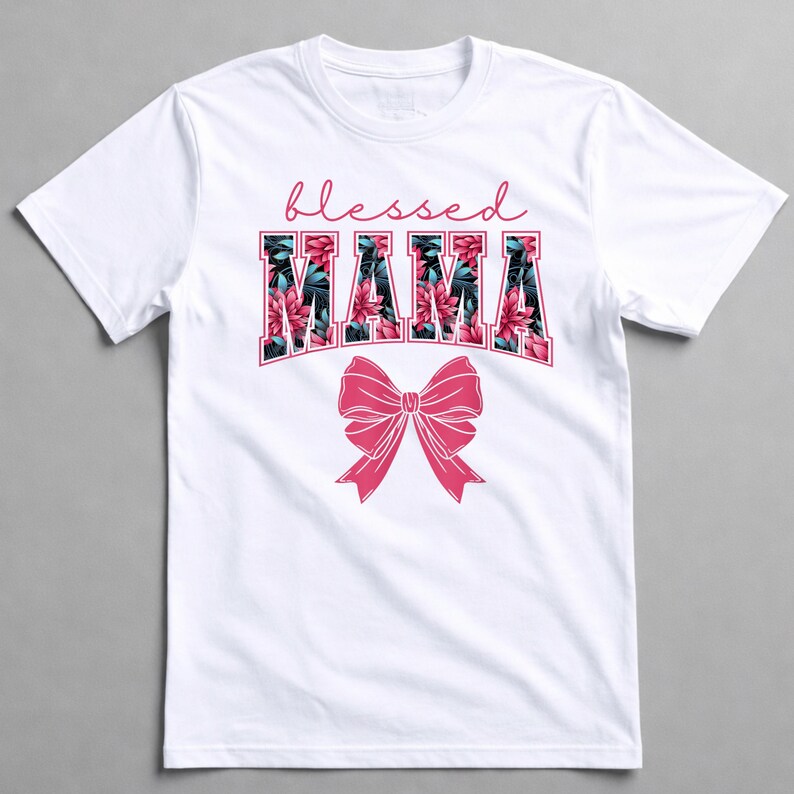 May include: White t-shirt featuring the text "blessed MAMA" in a floral design and a pink bow. The word "blessed" is in a cursive font above the word "MAMA". The floral design incorporates pink and green flowers.