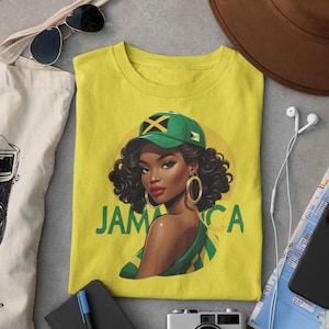 Peut inclure: T-shirt jaune avec un graphisme d'une femme portant une casquette verte avec le drapeau jamaïcain et des créoles dorées. Le mot "JAMAICA" est imprimé en vert. Lunettes de soleil, sac fourre-tout et chapeau visibles.