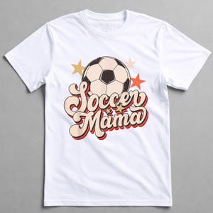 May include: White t-shirt featuring a soccer ball graphic and the text "Soccer Mama" in a retro font. The design includes gold and red stars. A casual, comfortable tee for soccer enthusiasts.