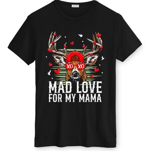 May include: Black t-shirt featuring a deer wearing a red cap and sunglasses with the text "XO XO". The deer's antlers are adorned with red heart shapes. The text "MAD LOVE FOR MY MAMA" is printed below the deer.